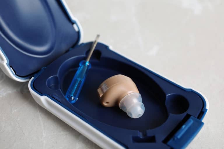 Case with hearing aid and small screwdriver on grey background, closeup