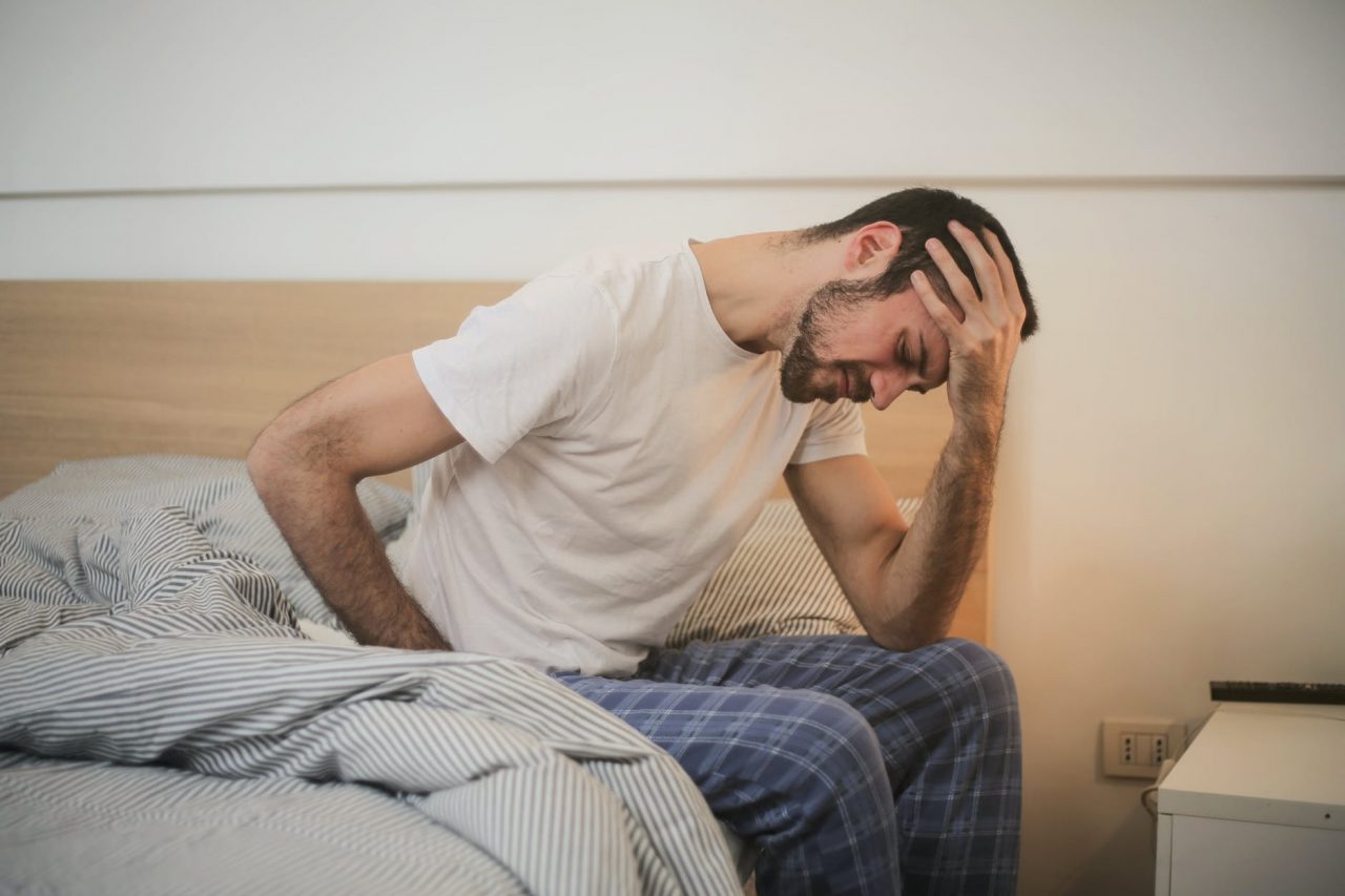 Tired man sitting on edge of bed.