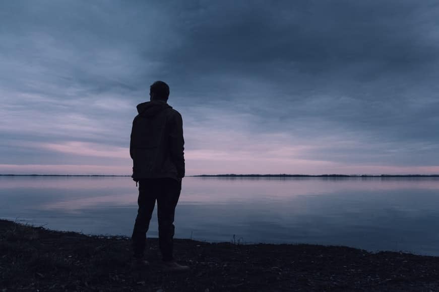 Silhouette of a man standing near a shore of water.