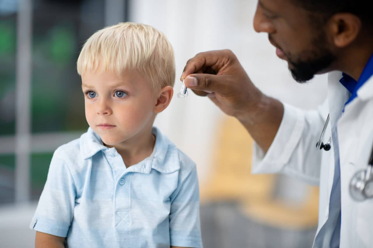 Doctor fitting a young boy with a pediatric hearing aid.
