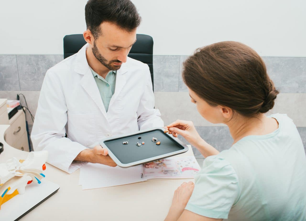 Audiologist showing a female patient a selection of hearing aids.