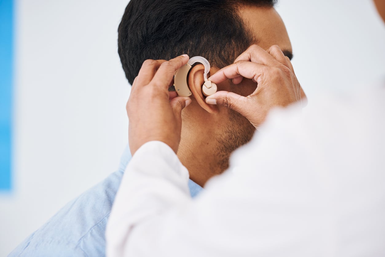 Audiologist putting a hearing aid in his patient's ear.