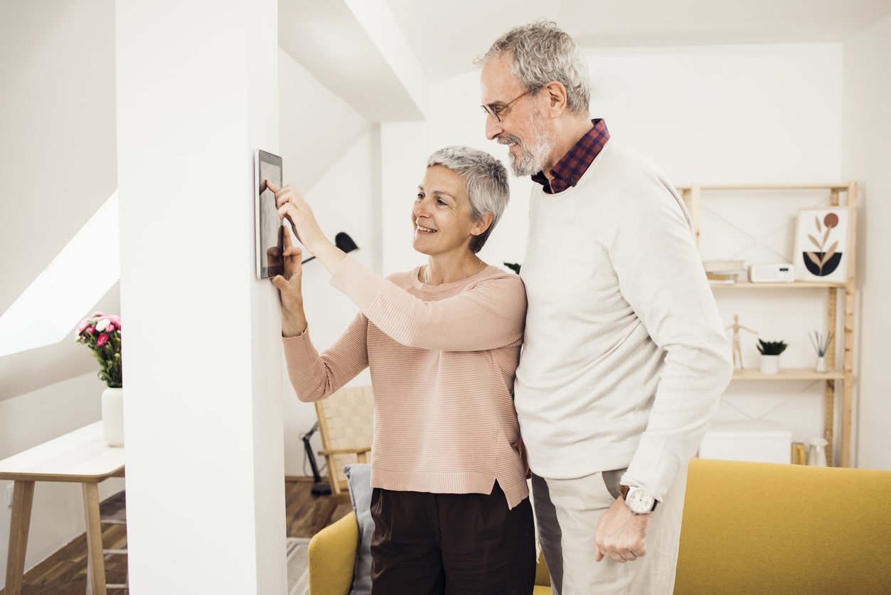 Senior couple adjusting home security settings on a wall tablet.