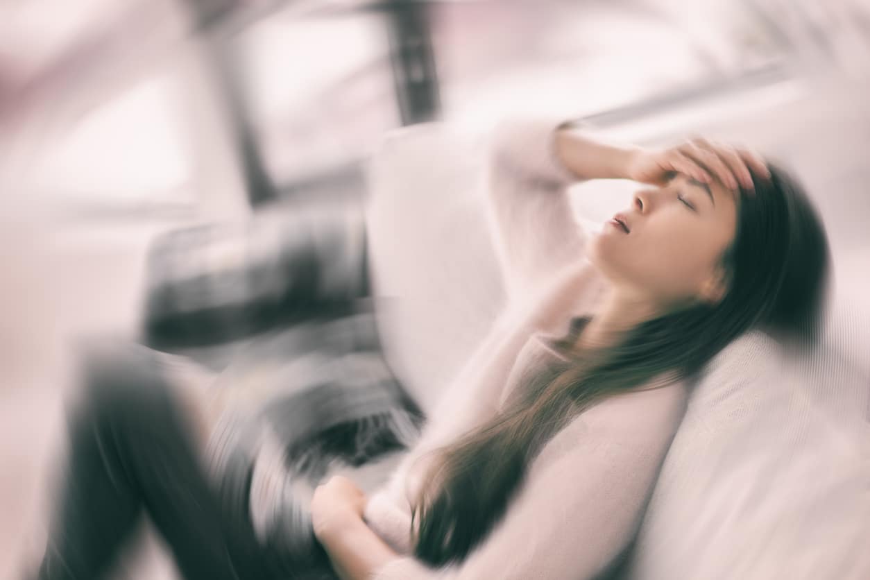 Woman with vertigo sitting on the couch feeling dizzy.